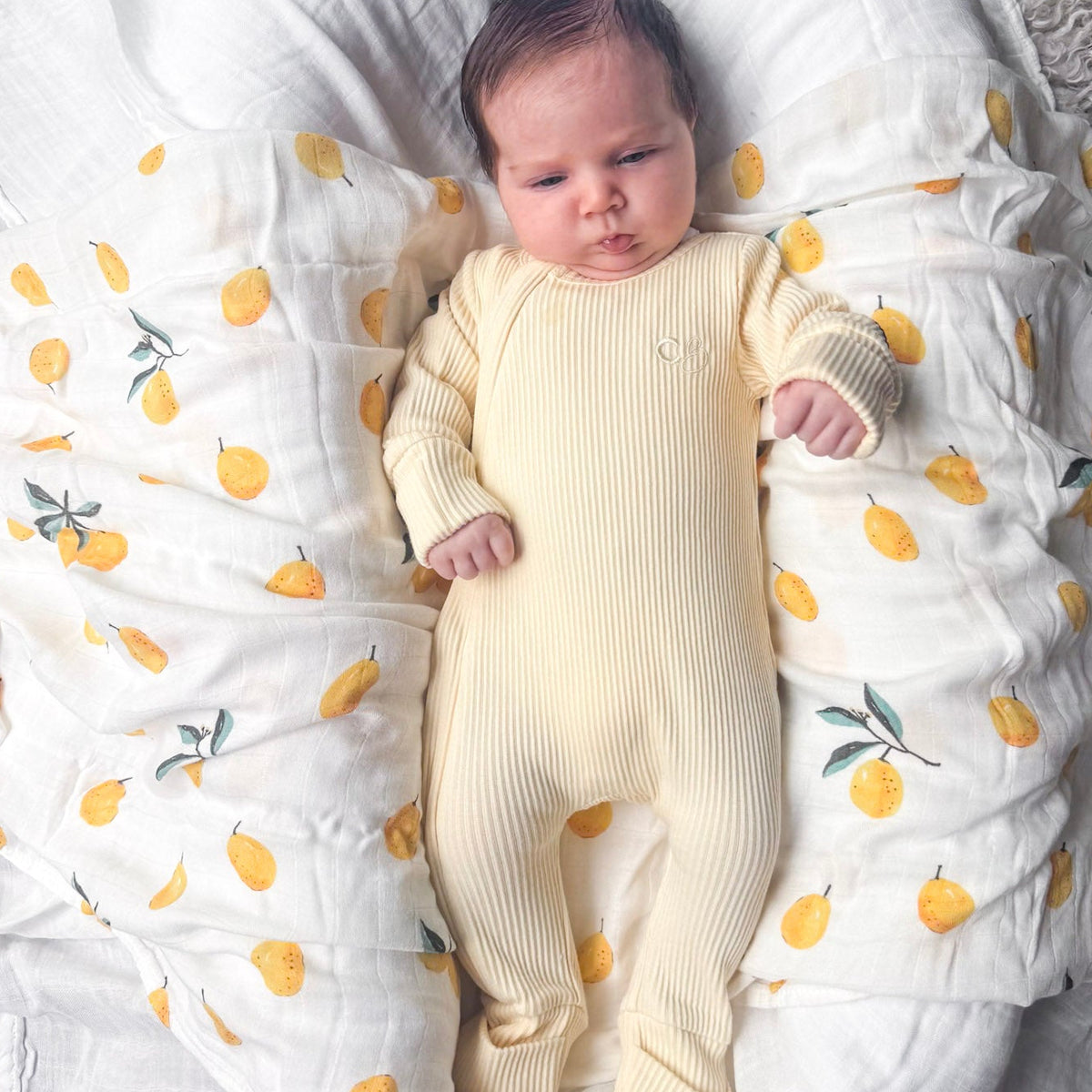 Newborn baby in a yellow onesie lying on a white blanket with lemon patterns