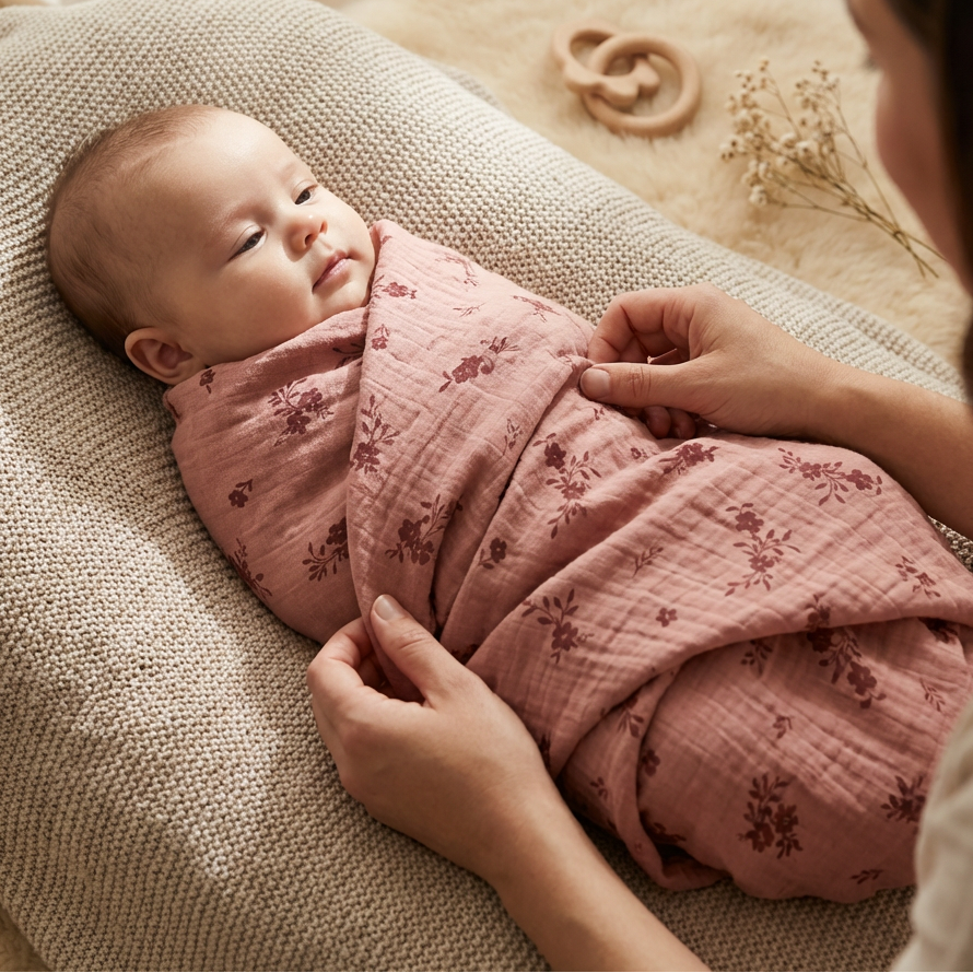 Baby wrapped in a pink floral swaddle blanket with a blurred background