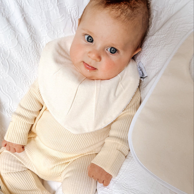 Baby in a cream-colored outfit lying on a white blanket with a lemon-patterned blanket.